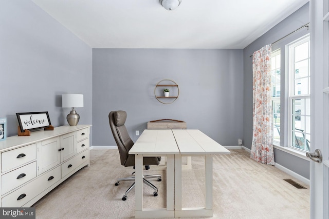 office area with baseboards, plenty of natural light, visible vents, and light colored carpet