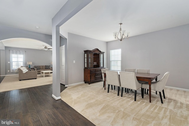 carpeted dining room featuring baseboards, arched walkways, wood finished floors, and ceiling fan with notable chandelier