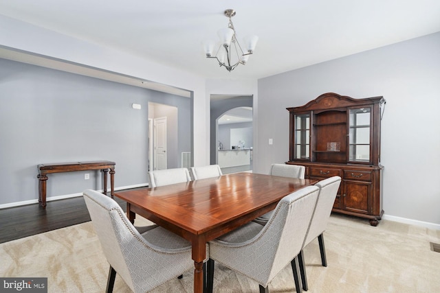 dining space featuring arched walkways, light colored carpet, a notable chandelier, visible vents, and baseboards