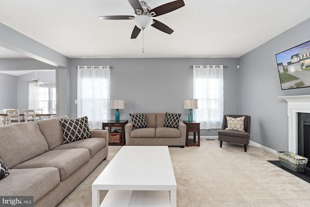 living area featuring light carpet, a fireplace with flush hearth, baseboards, and a ceiling fan