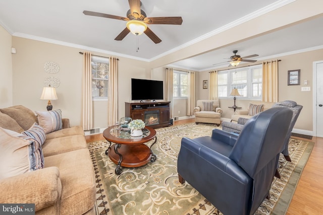 living room with baseboards, a ceiling fan, a glass covered fireplace, wood finished floors, and crown molding