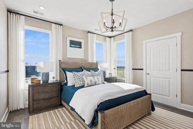 bedroom with baseboards, visible vents, an inviting chandelier, and wood finished floors