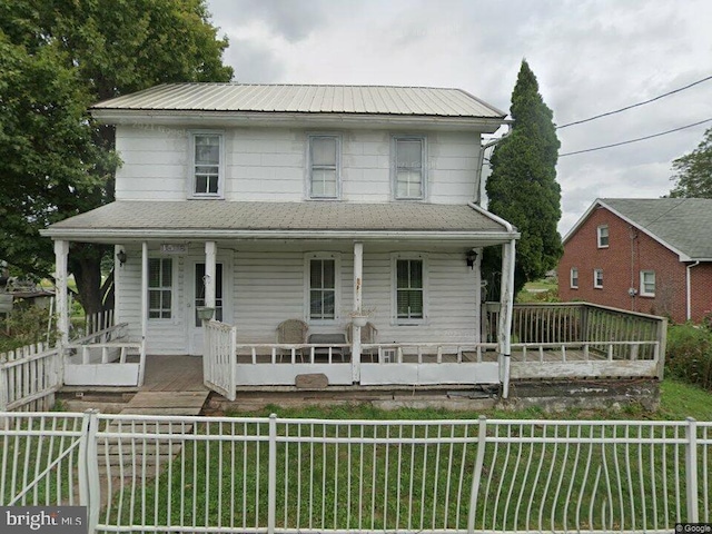 farmhouse with covered porch, metal roof, and a fenced front yard