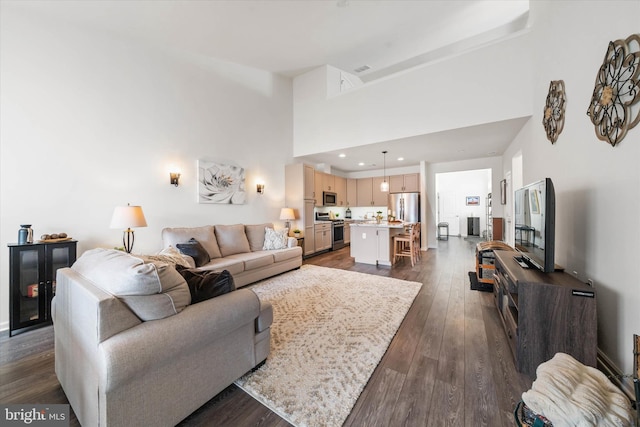 living area with recessed lighting, dark wood-style flooring, and a towering ceiling