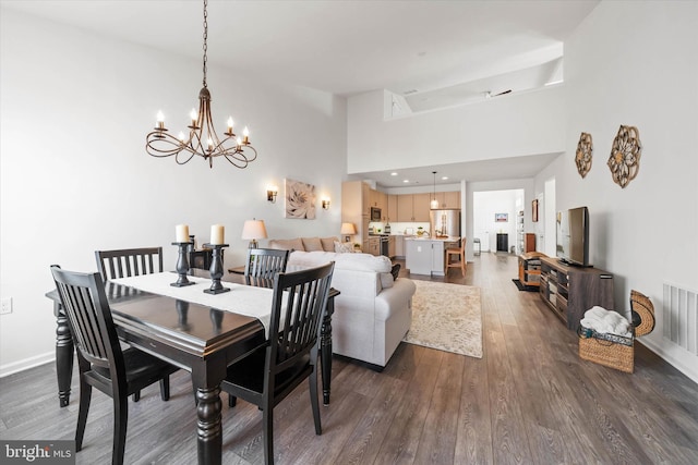 dining space featuring dark wood-style floors, visible vents, a high ceiling, a chandelier, and baseboards