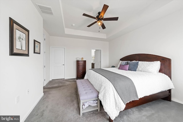 carpeted bedroom featuring ceiling fan, a tray ceiling, visible vents, and baseboards