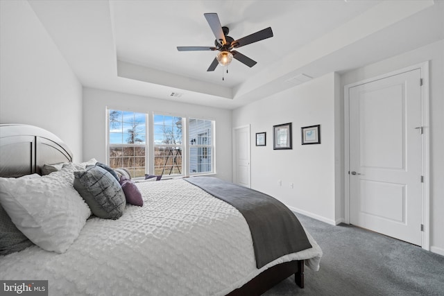 carpeted bedroom with baseboards, visible vents, a tray ceiling, and a ceiling fan