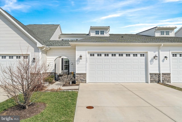 view of front facade featuring a garage, stone siding, driveway, and roof with shingles