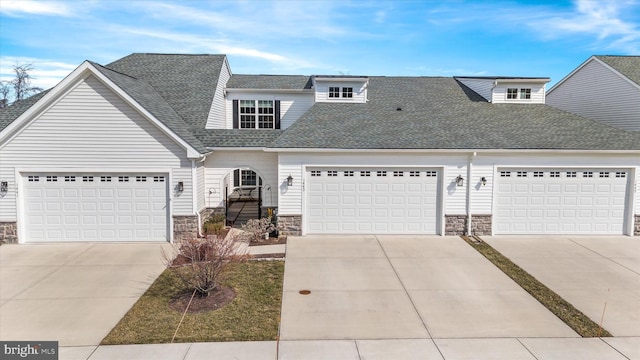 view of front of property with driveway, stone siding, a garage, and roof with shingles