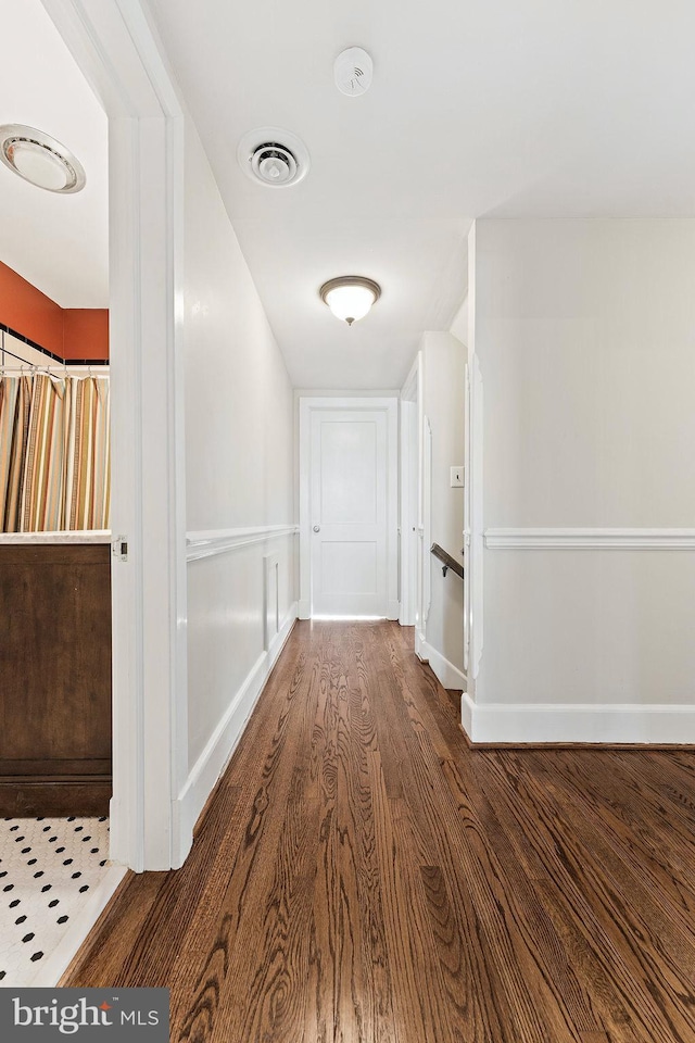 hall featuring wood finished floors, visible vents, and baseboards