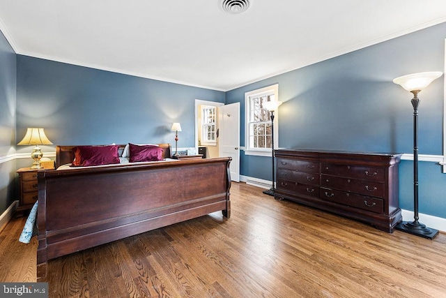 bedroom featuring wood finished floors, visible vents, and ornamental molding