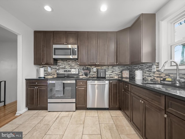 kitchen with light tile patterned flooring, a sink, dark brown cabinetry, appliances with stainless steel finishes, and backsplash