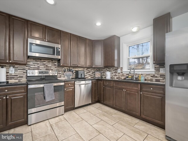 kitchen with a sink, stainless steel appliances, dark countertops, and dark brown cabinets