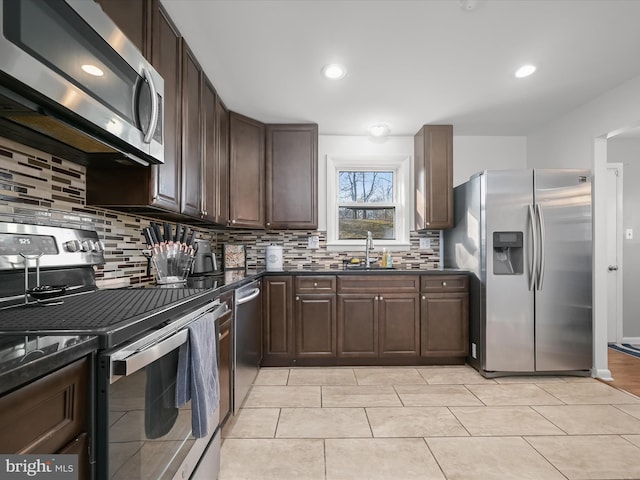 kitchen with dark countertops, tasteful backsplash, dark brown cabinetry, appliances with stainless steel finishes, and a sink