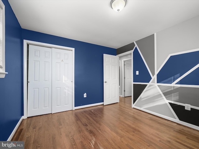 unfurnished bedroom featuring wood finished floors, a closet, and baseboards