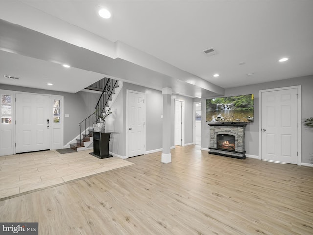 unfurnished living room featuring visible vents, a stone fireplace, wood finished floors, and stairs