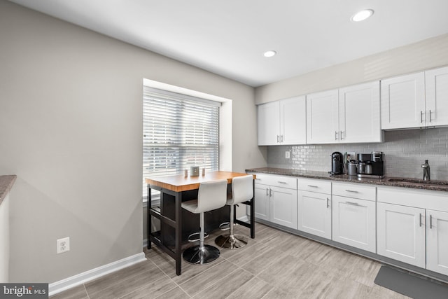 kitchen with a sink, decorative backsplash, white cabinets, and dark stone countertops