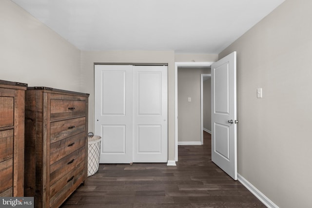 unfurnished bedroom featuring dark wood finished floors, baseboards, and a closet