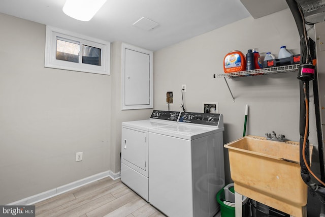 clothes washing area with a sink, washing machine and dryer, light wood finished floors, baseboards, and laundry area