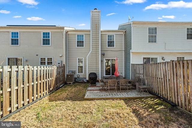 back of house with a lawn, cooling unit, a chimney, a fenced backyard, and a patio