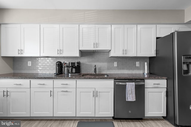 kitchen featuring light wood-type flooring, a sink, dark stone countertops, stainless steel appliances, and white cabinets