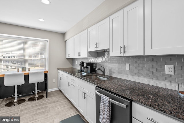 kitchen featuring white cabinetry, dark stone counters, a sink, dishwasher, and tasteful backsplash