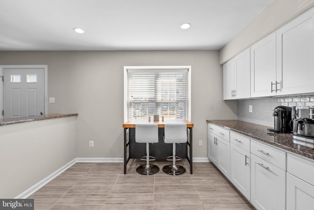 kitchen with backsplash, baseboards, recessed lighting, dark stone countertops, and white cabinetry