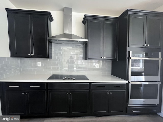 kitchen with wall chimney exhaust hood, double oven, and dark cabinets