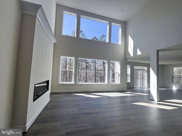 unfurnished living room with a towering ceiling, baseboards, and wood finished floors