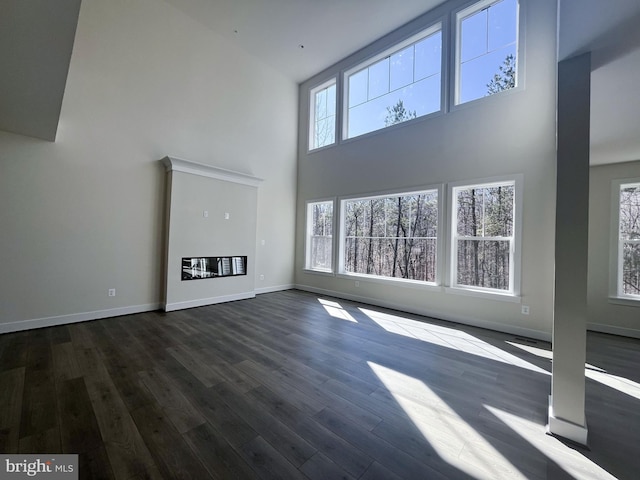 unfurnished living room with dark wood-style flooring, a towering ceiling, and baseboards