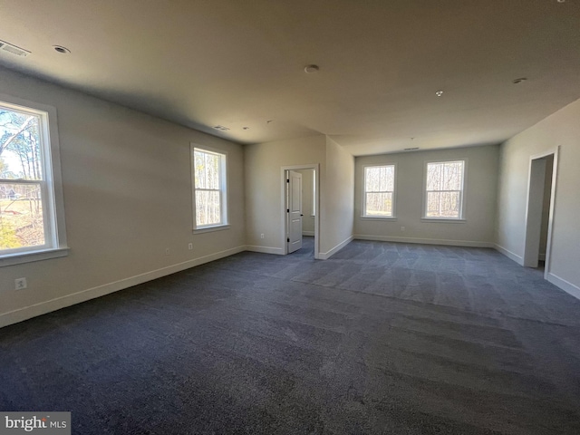 spare room featuring dark carpet, visible vents, and baseboards