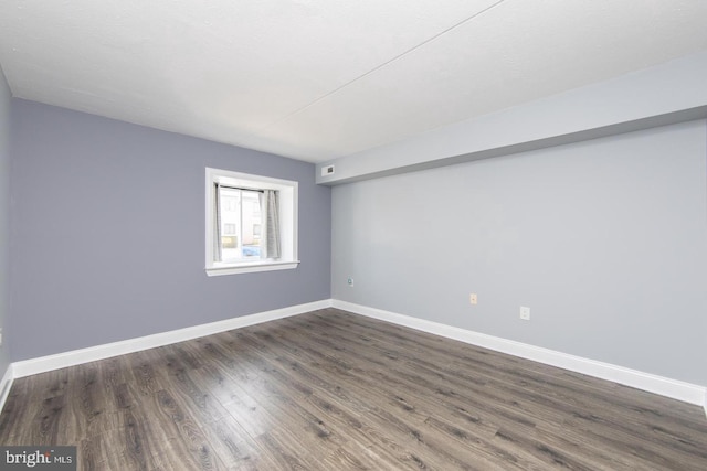spare room with dark wood-style flooring, visible vents, and baseboards