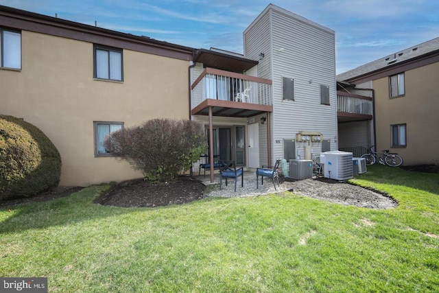 rear view of property with stucco siding, a lawn, central AC unit, a patio area, and a balcony