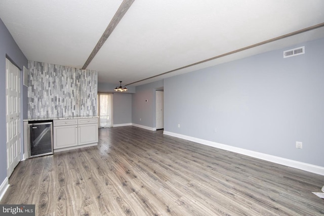 unfurnished living room featuring wine cooler, visible vents, baseboards, light wood-style floors, and an inviting chandelier