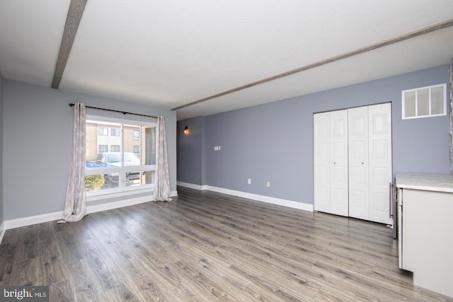 unfurnished living room featuring wood finished floors, visible vents, and baseboards