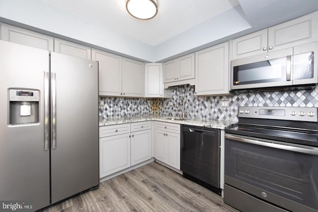 kitchen with stainless steel appliances, a sink, light wood finished floors, and decorative backsplash