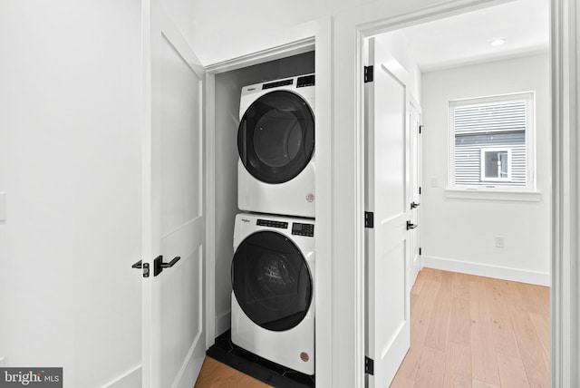 clothes washing area featuring light wood finished floors, laundry area, stacked washer / drying machine, and baseboards