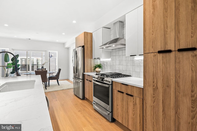 kitchen featuring decorative backsplash, stainless steel appliances, wall chimney range hood, and modern cabinets