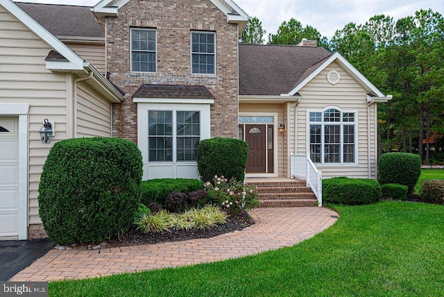 traditional home featuring a garage, a shingled roof, a chimney, a front yard, and brick siding