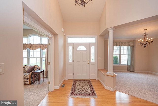 foyer entrance featuring decorative columns, light wood finished floors, visible vents, high vaulted ceiling, and baseboards