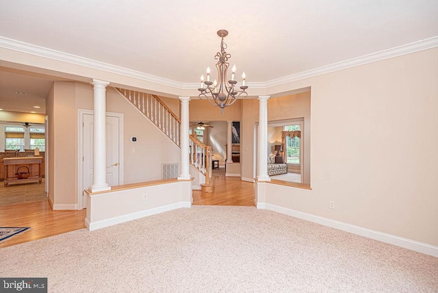 spare room featuring light colored carpet, ceiling fan with notable chandelier, stairway, ornate columns, and crown molding