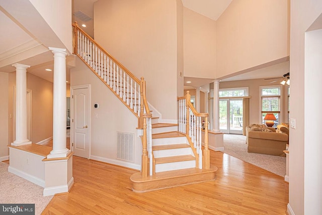 staircase featuring visible vents, decorative columns, a high ceiling, and wood finished floors