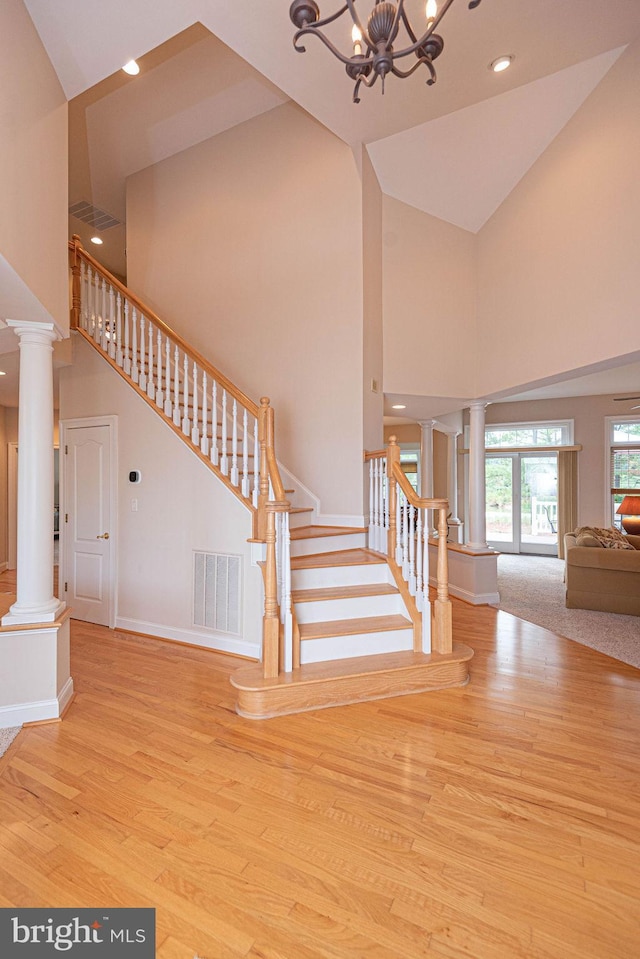 staircase featuring a towering ceiling, wood finished floors, visible vents, and ornate columns