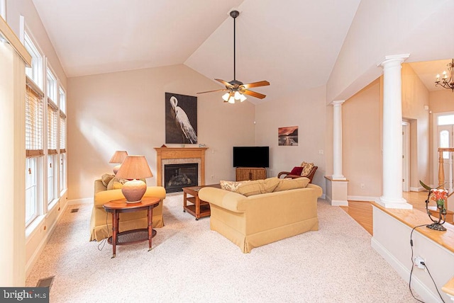 living room with a glass covered fireplace, vaulted ceiling, ornate columns, and ceiling fan with notable chandelier