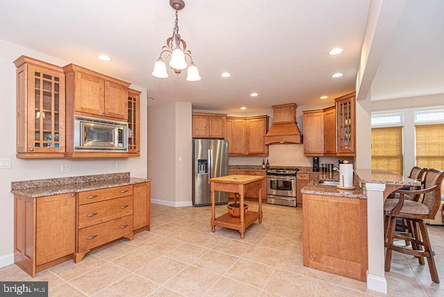 kitchen with a peninsula, a kitchen breakfast bar, appliances with stainless steel finishes, brown cabinetry, and custom range hood