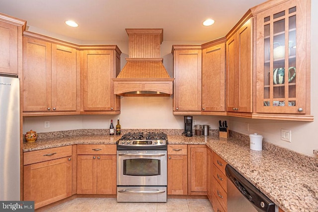 kitchen with custom range hood, glass insert cabinets, stainless steel appliances, and light stone counters