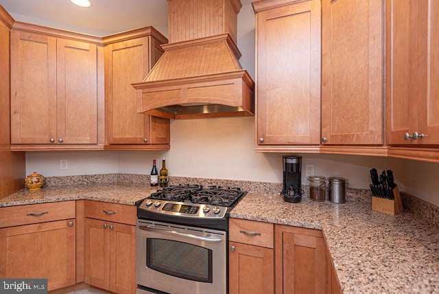 kitchen with stainless steel range with gas stovetop, custom exhaust hood, and light stone countertops