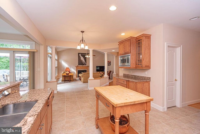 kitchen with brown cabinets, a fireplace, stainless steel microwave, a sink, and ornate columns