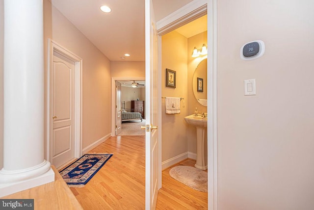 corridor featuring recessed lighting, baseboards, a sink, wood finished floors, and ornate columns