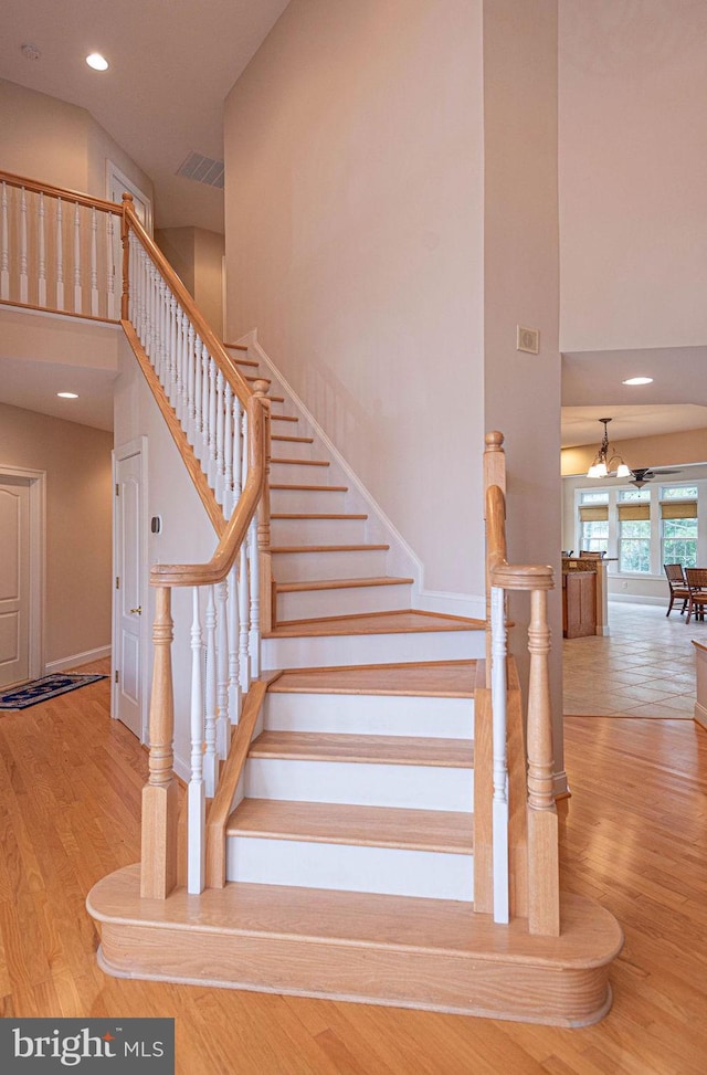 stairway featuring a high ceiling, wood finished floors, visible vents, and recessed lighting